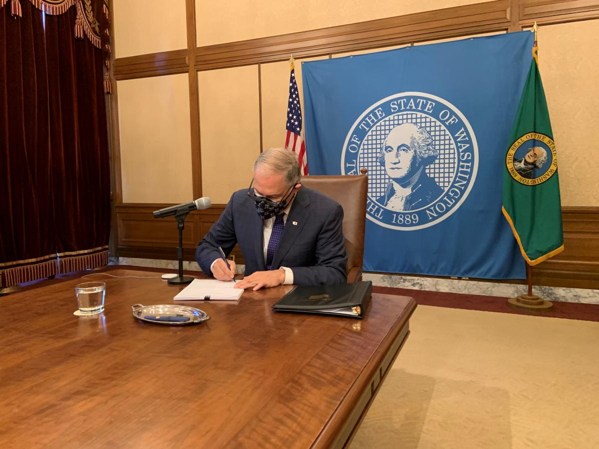 Gov. Inslee, seated at a conference room table, signs SB 5061.