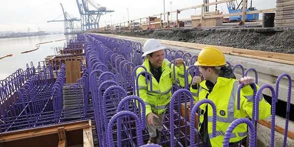 Two longshore-workers stand outside on a construction site at the Port of Tacoma, between steel rebar rods. 