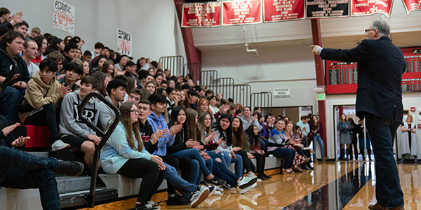 Governor Inslee addressing a group of students in the gym at Raymond High School. Governor Inslee is standing on the gym floor with students on the bleachers. 