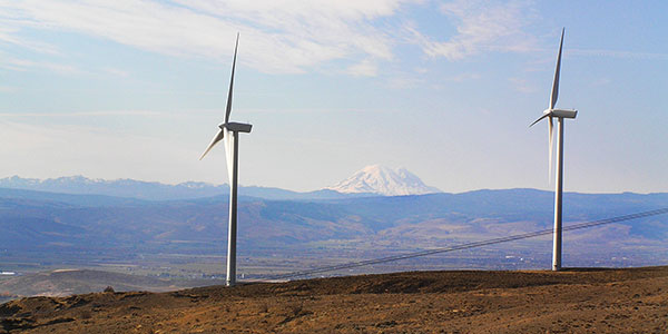 In the foreground, two windmills in a windmall farm in Vantage, Washington. Mt. Rainier can be seen in the distance in between the two windmills. e