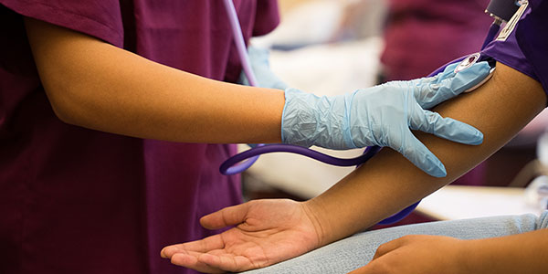 A close-up of a medical professional pressing the end of a stethoscope against a patient's under forearm. 