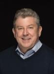 Bill Kehoe, a man, smiling wearing a Navy sweater over a patterned shirt