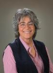 Cheryl Strange, a woman, smiling and wearing a black vest with a pink button-up shirt