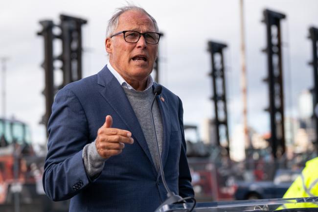 Inslee delivers a speech with large cranes behind him.