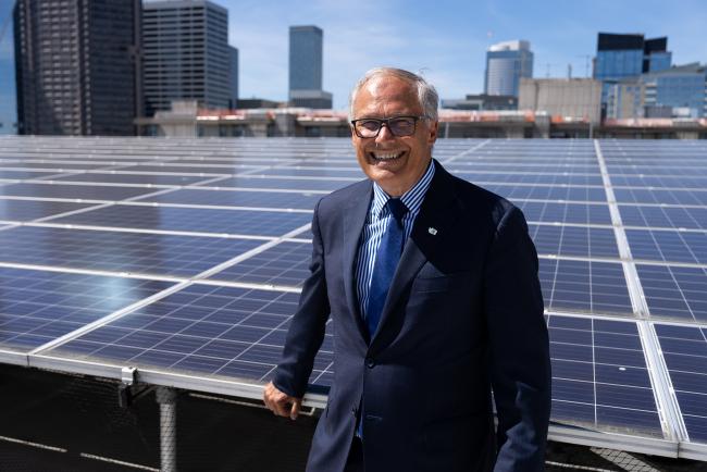 Gov. Jay Inslee smiles in front of a rooftop solar panel installation.