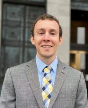 Headshot of Beau wearing a an suit, blue shirt, and patterned tie